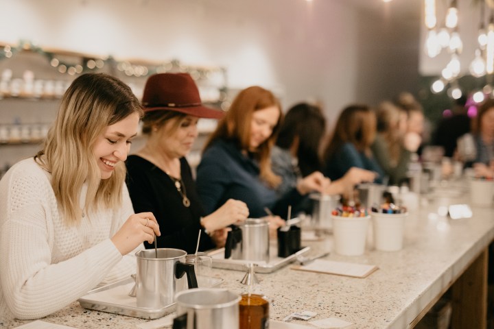People sitting at a long table making candles indoors.