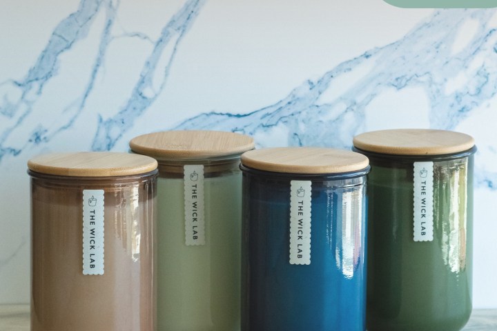 Four colored candles with wooden lids against a marble backdrop.