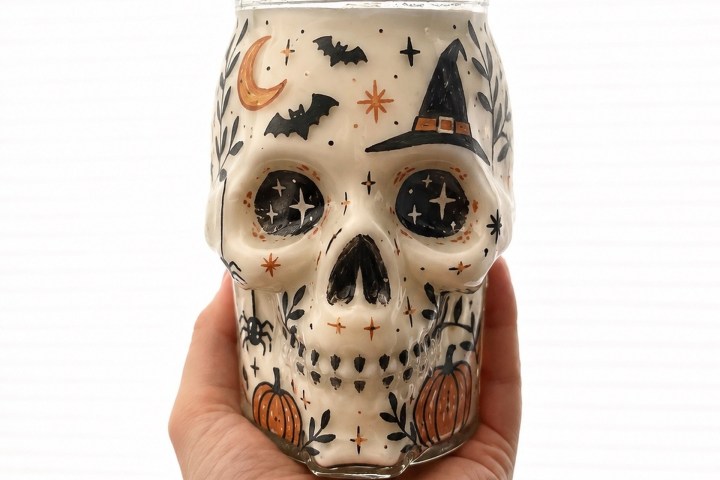 Hand holding skull-shaped jar with Halloween motifs.