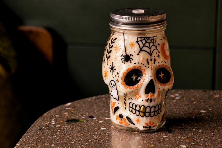 Decorative skull jar with Halloween motifs on a speckled table.